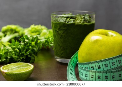 Measuring tape around an apple. Green smoothie in glass. Lime and lettuce leaves on table. Close up. Grey background - Powered by Shutterstock