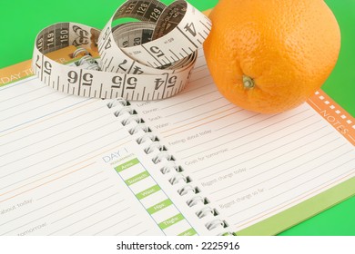 A Measuring Tape, Diet And Nutrition Journal And An Orange