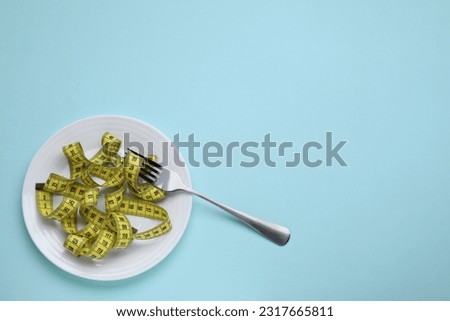 Measuring tape and fork on light blue background, top view with space for text. Weight loss concept