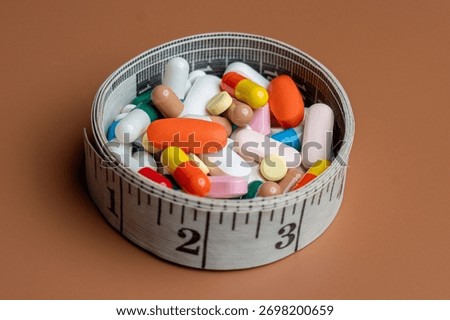 A measuring tape forms a circular container filled with a variety of colorful pills and capsules. Diet pills, weight loss supplements, and medical dosage control concepts.