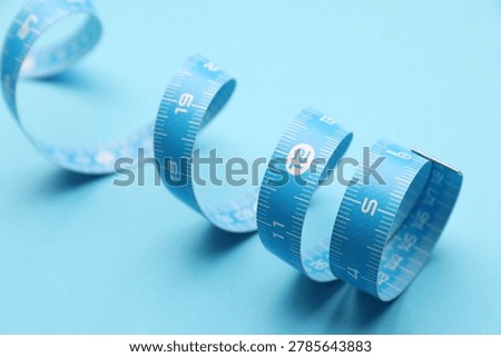 Measuring tape on light blue background, closeup
