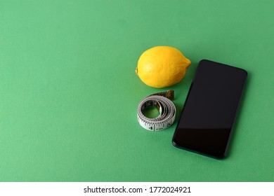 Measuring tape roll, smartphone and ripe yellow lemon on a green background. Concept of healthy eating, diet, weight loss and body slim. Copy space. 
