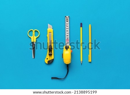 Measuring tape, scissors, knife, pen and pencil on a blue background. A set for creativity of yellow color. Flat lay.