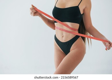 With measuring tape. Woman in underwear with slim body type is posing in the studio.