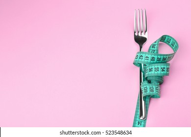 Measuring tape wrapped around fork lying on color surface. Diet concept - Shutterstock ID 523548634