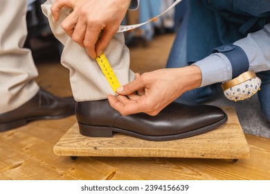 Measuring trouser length with tape on man's ankle above brown shoe