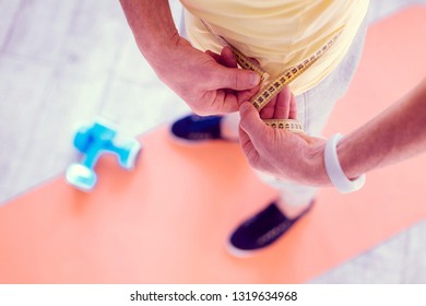 Measuring waistline. Mature athletic strong man wearing white smart watch on his hand measuring his waistline - Powered by Shutterstock