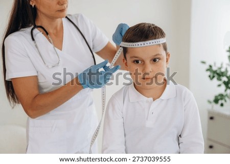 Measuring the width of head. Boy is in routine appointment in clinic with female doctor.