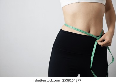 Measuring a woman's waist with a tape measure, focusing on body positivity and healthy weight management. - Powered by Shutterstock