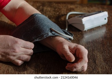 Measuring Your Blood Pressure At Home. An Adult Male Puts A Digital Blood Pressure Monitor Cuff On His Forearm. Inside The Room. Selective Focus.