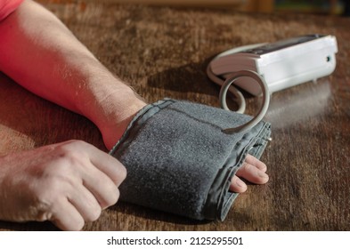 Measuring Your Blood Pressure At Home. An Adult Male Puts A Digital Blood Pressure Monitor Cuff On His Forearm. Inside The Room. Selective Focus.