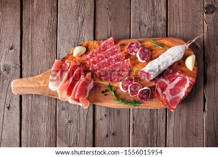Meat appetizer platter with sausage, prosciutto, ham and salami. Top view on a serving board against a wood background.