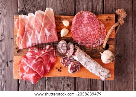 Meat appetizer platter with sausage, prosciutto, ham and salami. Overhead view on a serving board against a wood background.