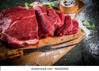 Meat. Beef, veal. Fresh raw tenderloin, piece without bone. For frying grilling barbecue. Cut into steaks, whole. On black stone table,cutting board, spices, salt, fork for meat. Top view copy space 