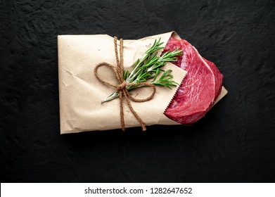 
Meat From A Butcher Shop, Wrapped In Paper. A Piece Of Beef On A Concrete Black Background