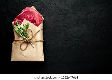 
Meat From A Butcher Shop, Wrapped In Paper. A Piece Of Beef On A Concrete Black Background