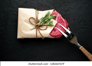 
Meat From A Butcher Shop, Wrapped In Paper. A Piece Of Beef On A Concrete Black Background