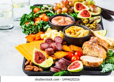 Meat And Cheese Appetizer Platter. Sausage, Cheese, Hummus, Vegetables, Fruits And Bread On A Black Tray, White Background.