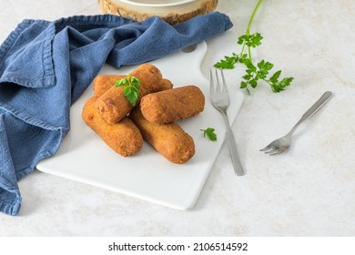 Meat croquets and parsley leaves on white ceramic dishes in a kitchen counter top.