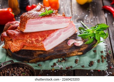 Meat delicacy, boiled pork beautiful, whole or sliced on a kitchen cutting board, spices and vegetables, dark and moody, clouseup on a black wooden isolated background, top	
					