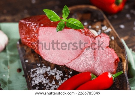 Meat delicacy, boiled pork beautiful, whole or sliced on a kitchen cutting board, spices and vegetables, dark and moody, clouseup on a black wooden isolated background, top	
