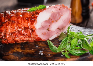 Meat delicacy, boiled pork with layers of lard, whole or sliced on a kitchen cutting board, spices and vegetables, dark and moody, clouseup on a black wooden isolated background, top