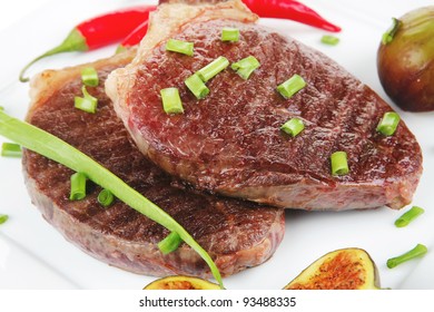 meat entree : grilled beef steak served with red hot cayenne peppers green chives and sweet figs on plate isolated over white background