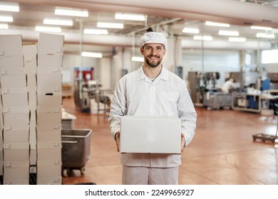 A meat factory laborer is carrying box with meat products and getting ready for shipping while smiling at the camera. - Powered by Shutterstock