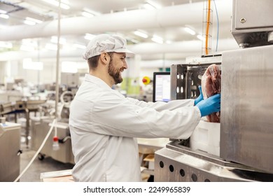 A meat factory laborer is putting piece of fresh meat into a meat grinding machine. - Powered by Shutterstock