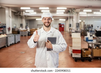 A meat factory quality inspector is giving thumbs up for excellent quality of products while holding tablet and smiling at the camera. - Powered by Shutterstock