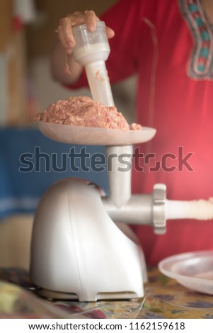 Meat grinder with fresh forcemeat and woman making sausages in kitchen