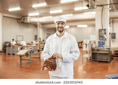 A meat industry worker is holding piece of fresh meat and smiling at the camera. - Powered by Shutterstock