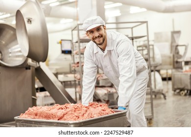 A meat industry worker is pushing a container with ground meat while smiling at the camera. - Powered by Shutterstock