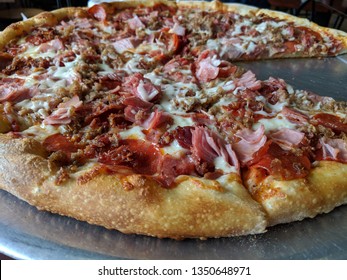Meat Lovers Pizza Pie with One Slice Missing, Many Meat Toppings Including Pepperoni, Ham, Bacon, Sausage, and Beef with Red Sauce and Mozzarella on a Round Silver Platter