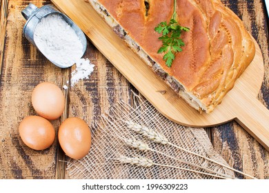 Meat Pie On A Wooden Table, Eggs And Flour Next To The Pie. View From Above