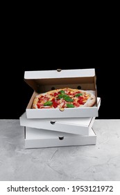 meat pizza inside box. stack of pizza boxes standing on concrete table and black background.