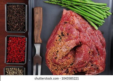 meat raw beef fillet chunk on black tray asparagus on wooden table allspice pink white black green peppercorn