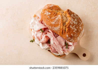 Meat sandwich with whole wheat bread prosciutto cotto, italian ham and soft cream cheese on a small wooden bread. Light beige background, directly above.