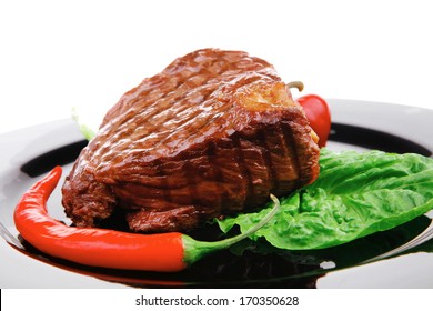 meat savory : beef grilled and garnished with green lettuce and red chili hot pepper on black dish isolated over white background