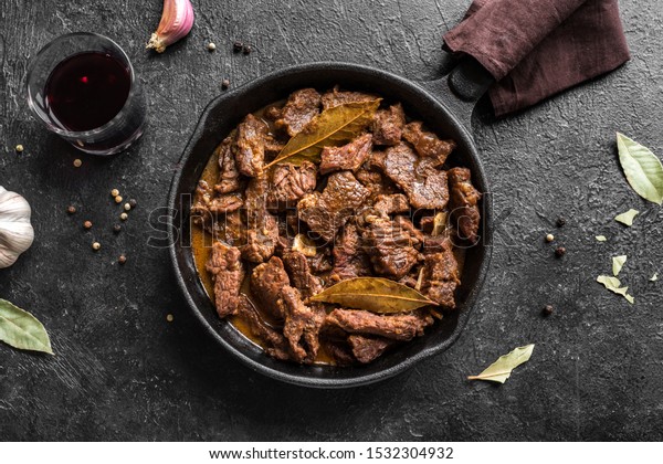 Meat Stew. Beef stewed in red wine sauce, top view,\
copy space. Roasted beef meat. Braised beef portion meat. Slow\
cooked meat in cast iron\
pan.