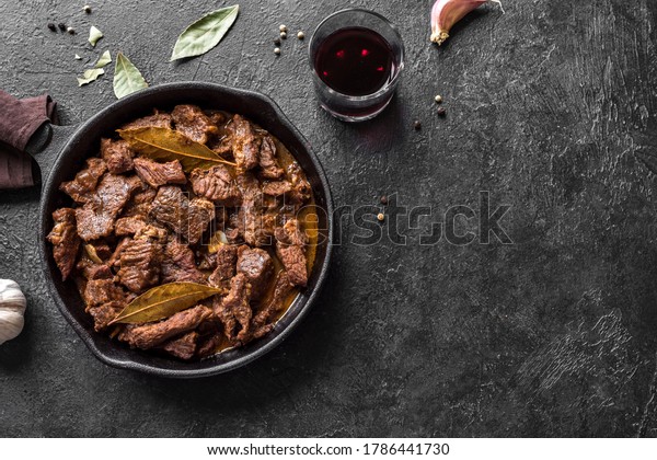 Meat Stew. Beef stewed in red wine sauce, top view,\
copy space. Roasted or braised beef meat. Slow cooked meat in cast\
iron pan.
