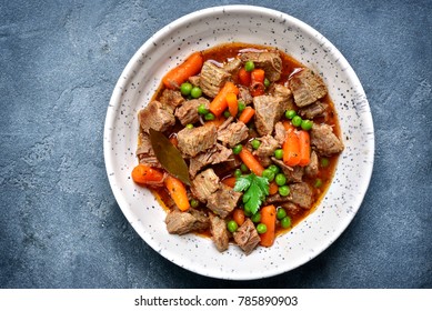 Meat stew with carrot and green pea in a white bowl over dark grey slate or stone background.Top view.