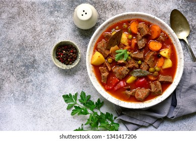 Meat stew with vegetables in tomato sauce in a white bowl on a light grey slate, stone or concrete background.Top view with copy space.