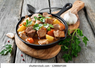  Meat stewed with potatoes, carrots and spices in iron pan on wooden background .