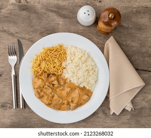 Meat strogonoff with rice and straw potato over wooden table.