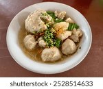 Meatballs in a bowl with vegetables and noodles on the table. Meatballs served with noodles, a soupy dish with ground meat shaped into balls, a typical Indonesian food.