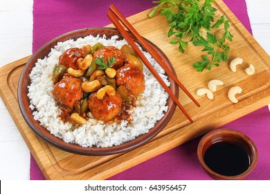 Meatballs Stewed In Sauce Of Green Bell Pepper, Onion, Soy Sauce, Chinese Cooking Wine, Cashew Nuts And Spices Served On Basmati Rice On Clay Dish On Wooden Board With Chopsticks, Close-up