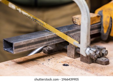 Mecanicien aserrando una barra de metal fijada en el vicio con una sierra manual