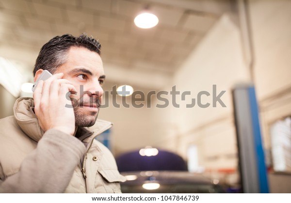 mechanic answers a phone call while checking\
vehicle levels in a mechanic\
workshop