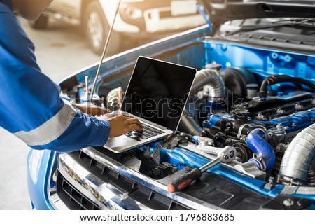 Mechanic Asian man close up using laptop computer examining tuning fixing repairing car engine automobile vehicle parts using tools equipment in workshop garage support service in overall work uniform